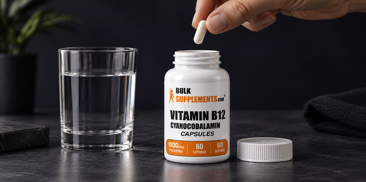 Mano sosteniendo una cápsula de Vitamina B12 junto a un vaso de agua